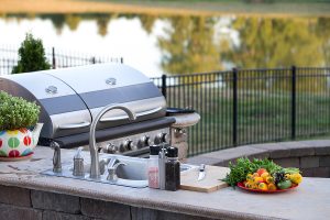 An outdoor kitchen with a counter top, sink, and grill overlooking pond to accentuate the advantages of having an outdoor kitchen