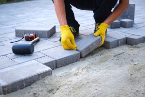 A mason placing concrete pavers to form and outdoor patio