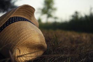 Summer straw hat with blue ribbon and dots lay at dry end summer grass.