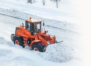 Large orange tractor plowing snow in snowstorm.